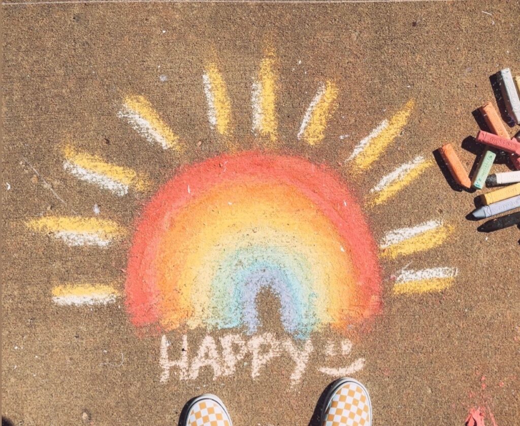 chalk drawing of a rainbow with word happy and smiley face drawn