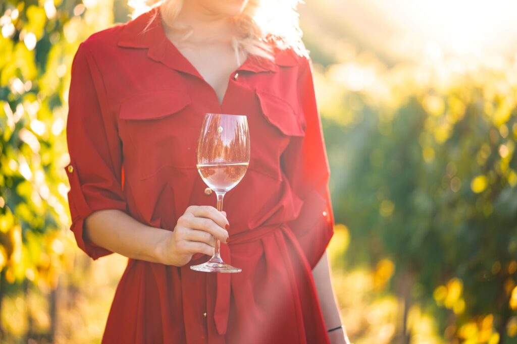 Woman wearing red dress holding a glass of wine and standing in a vineyard