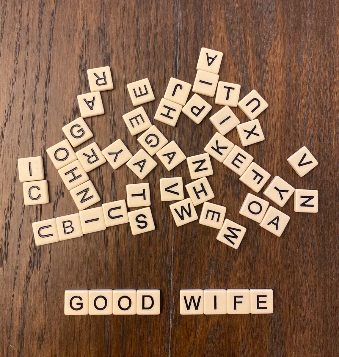 scattered scrabble tiles on brown wooden surface spelling good wife