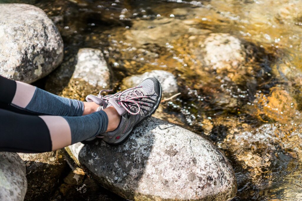 woman's legs in workout leggings as she sits on a rock by a stream