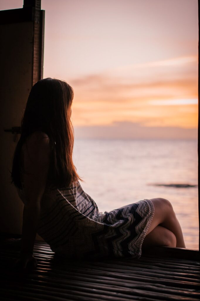 Woman in black and white dress sitting on window during sunset
