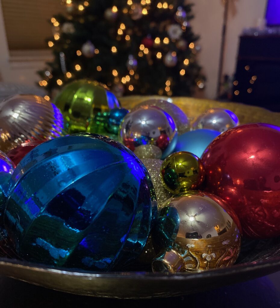 Bowl of colored , round Christmas decorations with tree in the background