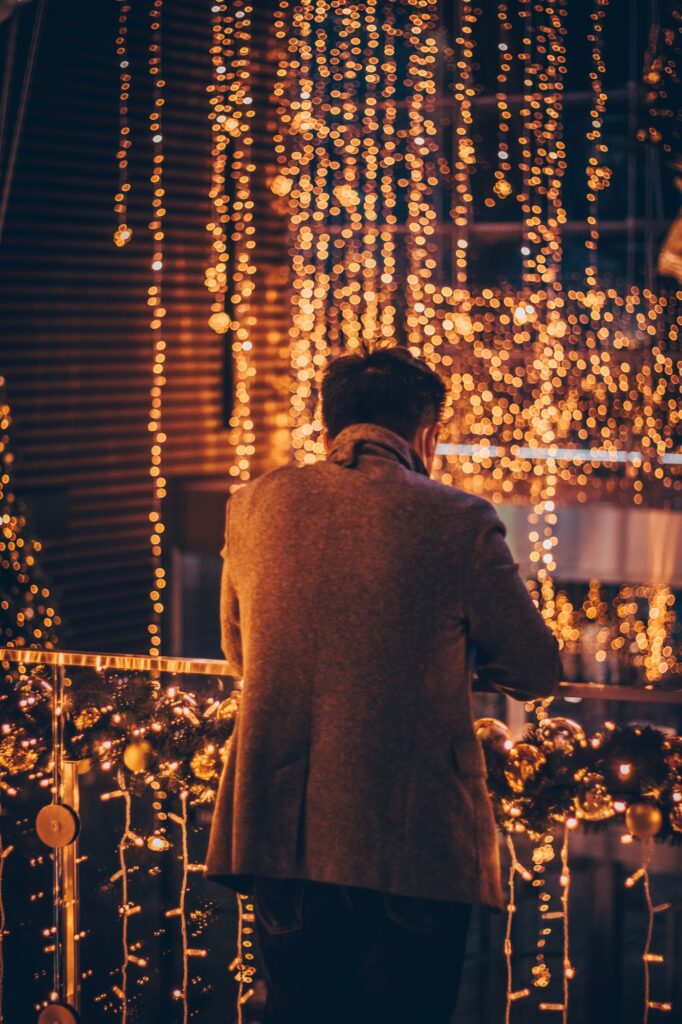 Back of a man in a brown coat facing  strings of Christmas lights