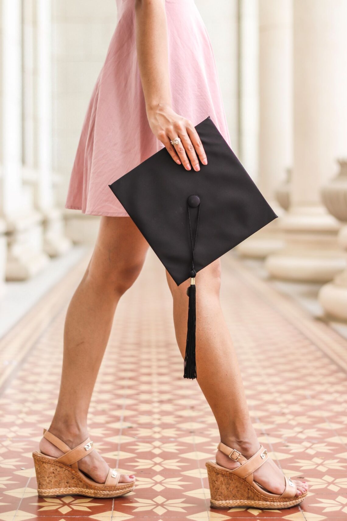 cropped woman in pink dress holding graduation hat