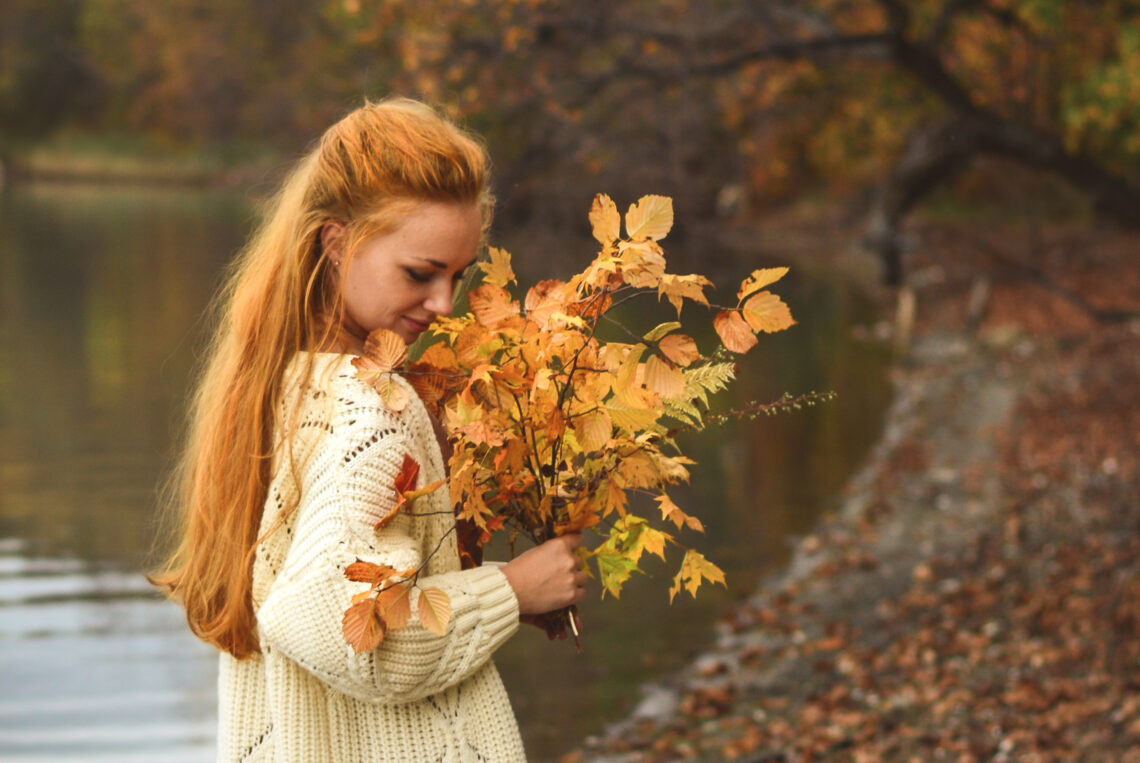 Woman carrying brown leaves standing near water