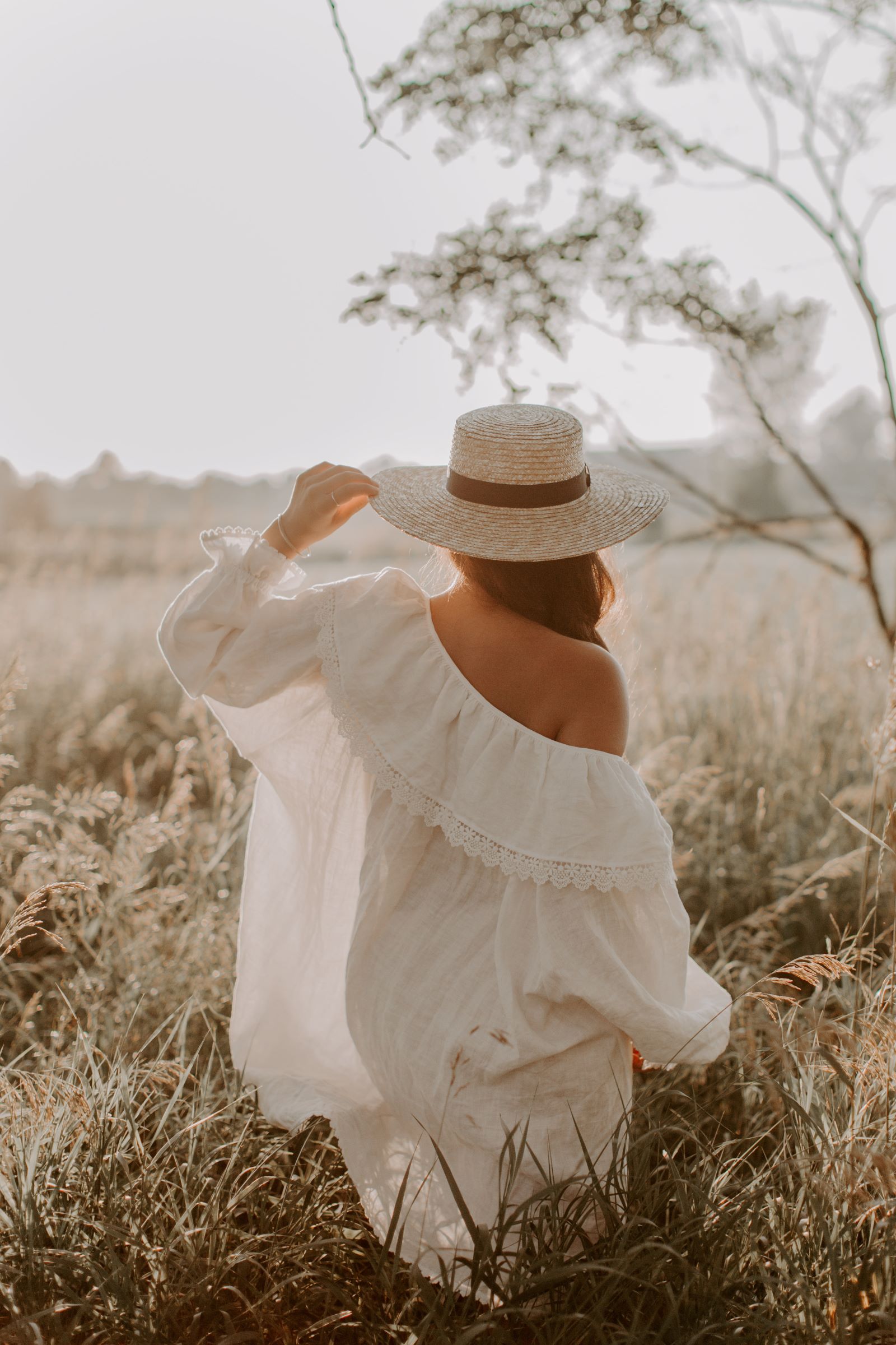 back of woman wearing white dress and hat in a field