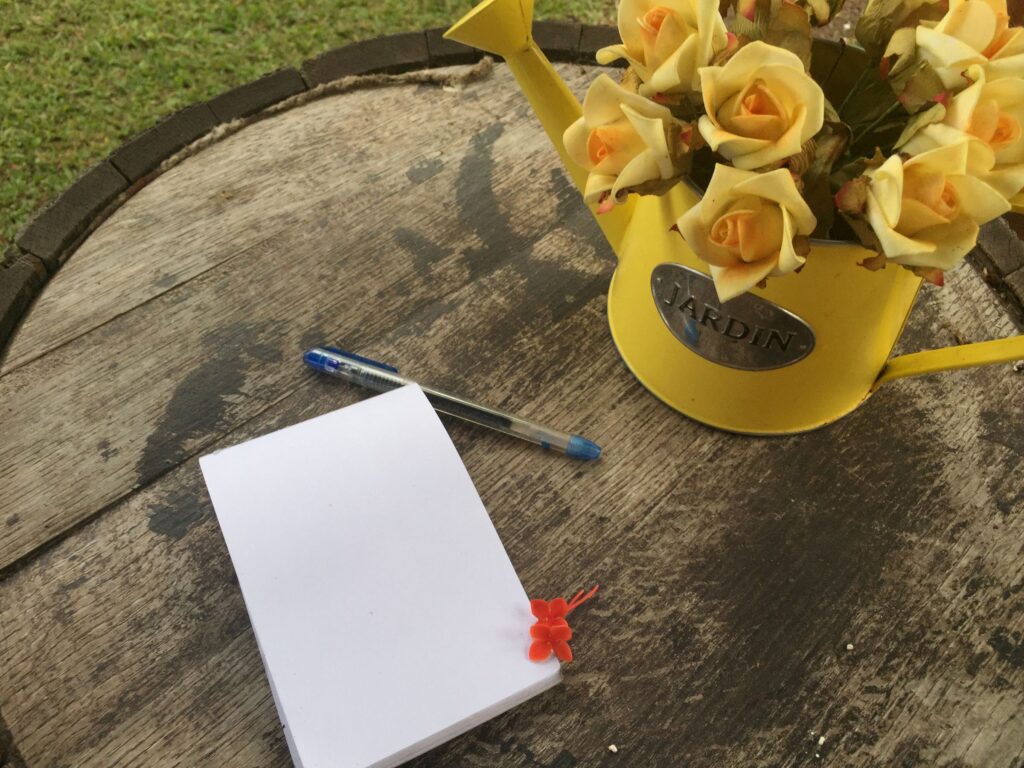Journal on a table outdoors with pen and yellow vase with yellow flowers in it
