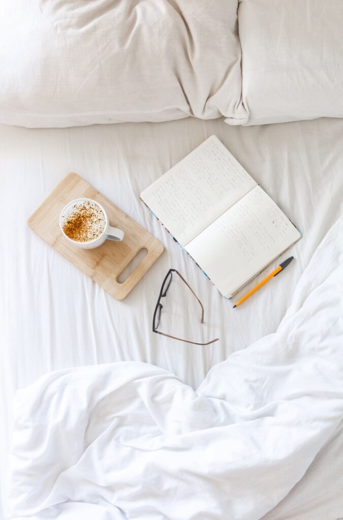 Journal laying on a bed next to a cup of coffee, glasses and a pen