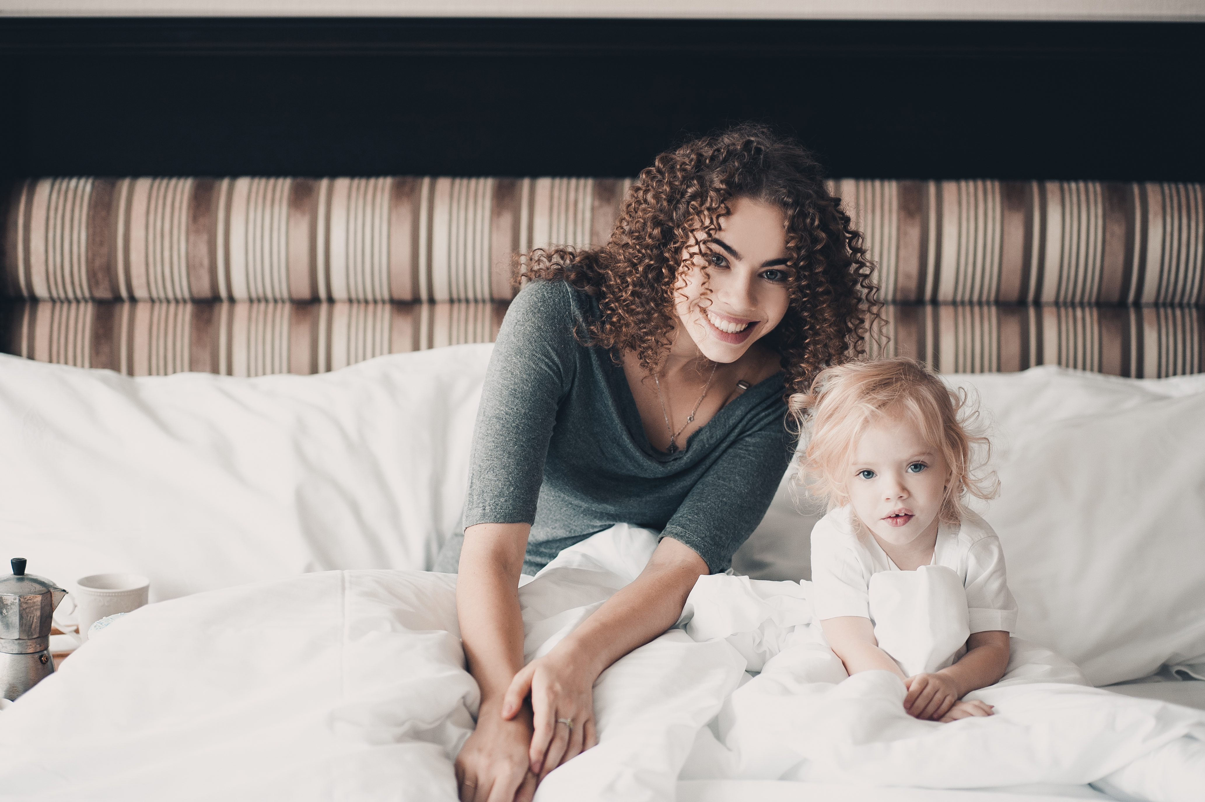 Woman in gray shirt holding baby on bed